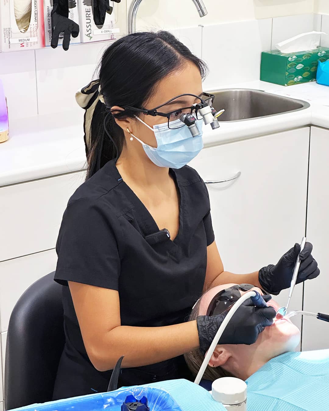 Dr. Sein performing clinical dental care at Beyond Dental Care Hamilton, using magnification loupes during a patient appointment.