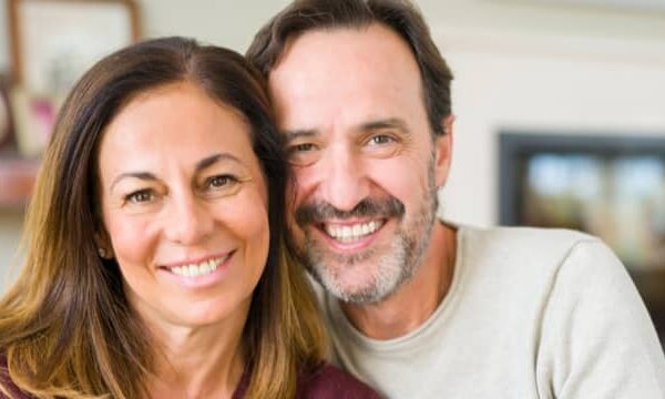 Happy senior couple smiling confidently after receiving dental implants and bridges for a complete smile restoration.