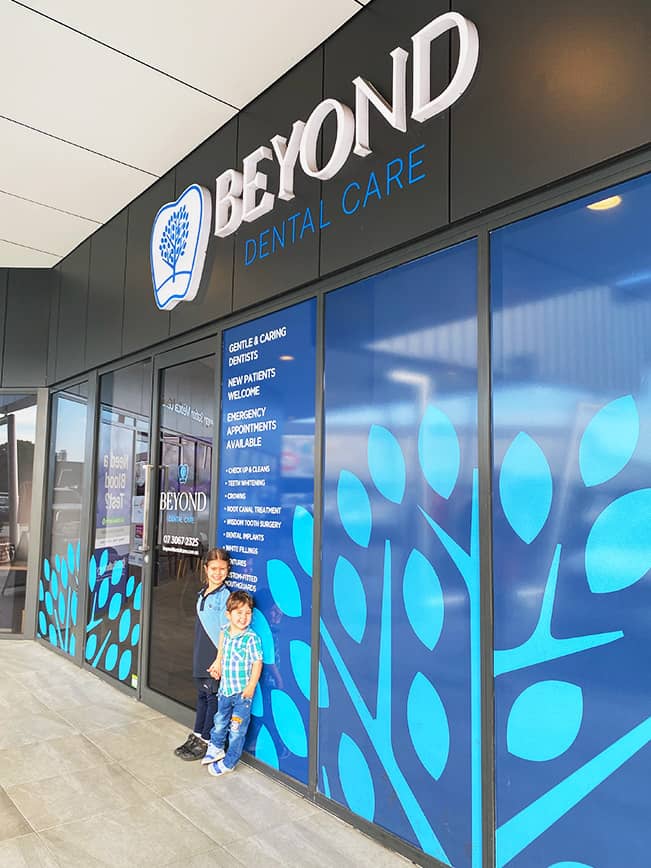 A brother and sister beam with healthy smiles outside Beyond Dental Care, excited about their positive dental experience.