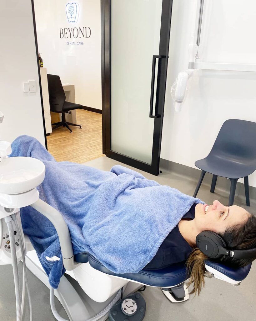 A patient listens to calming music with noise-cancelling headphones. This reduces ambient noise by up to 70%, minimising auditory triggers of dental anxiety. One of the most popular comfort items at our Bellara dental clinic