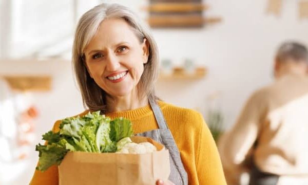 Woman with titanium dental implants smiling confidently while holding a bag of groceries, enjoying her daily routine.