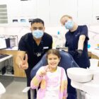 Paediatric dentist Dr Div and dental assistant smiling with happy girl patient showing OK sign at Beyond Dental Care clinic