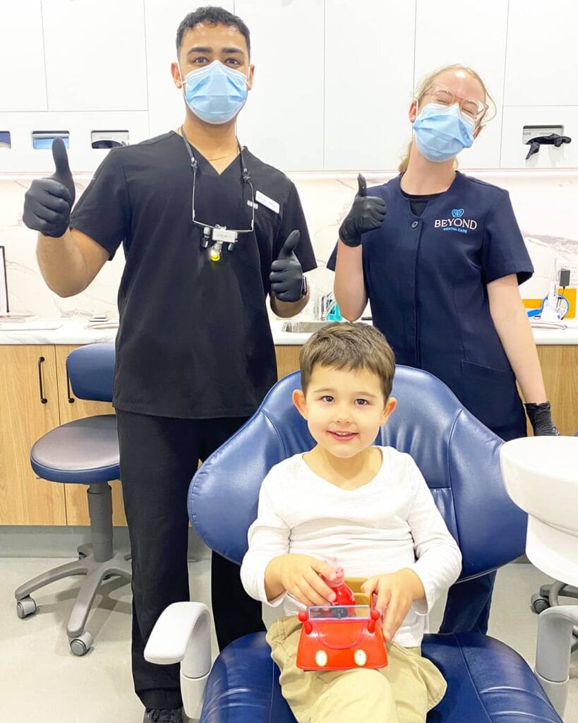Our Paediatric dentist Dr Div and caring dental team Dr Div paediatric dentist and dental assistant with smiling boy holding toy car after checkup and clean at Beyond Dental Care
