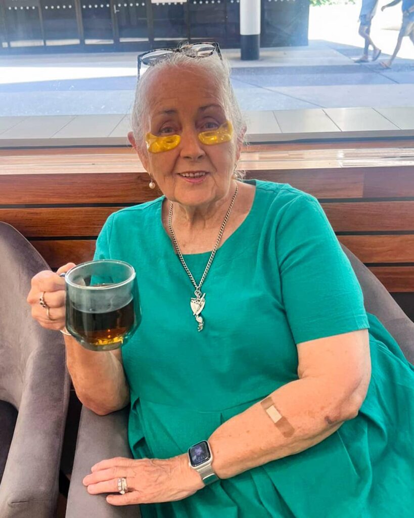 Herbal Tea and 24K Gold Gel Collagen Eye Pads A senior patient wearing 24K Gold Gel Collagen Eye Pads while smiling and holding a glass mug of herbal tea.
